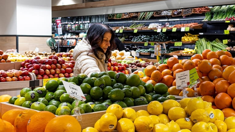 A woman browses produce for sale at a grocery store,...