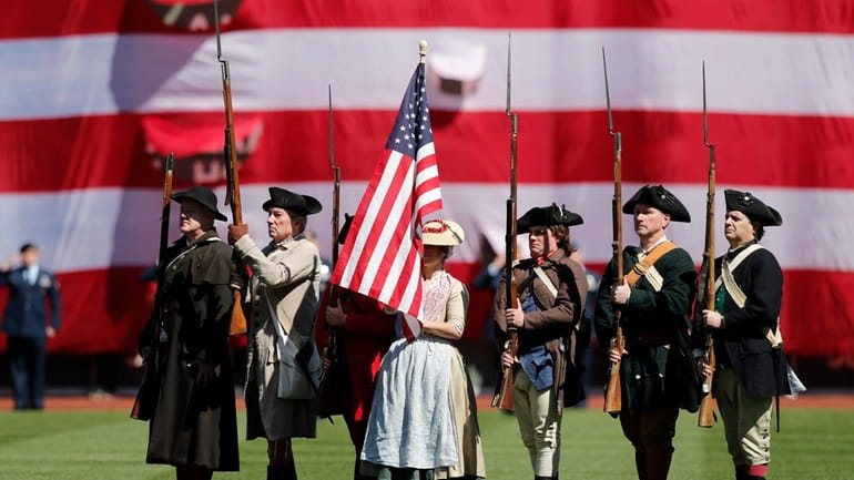 Colonial era re-enactors stand for the national anthem before a...