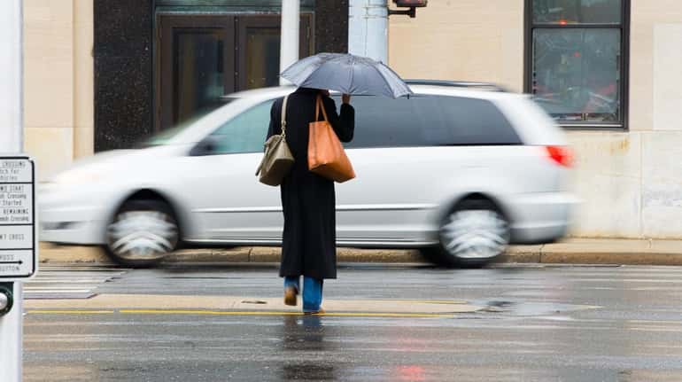 A woman with an umbrella crosses Sunrise Highway in Rockville...
