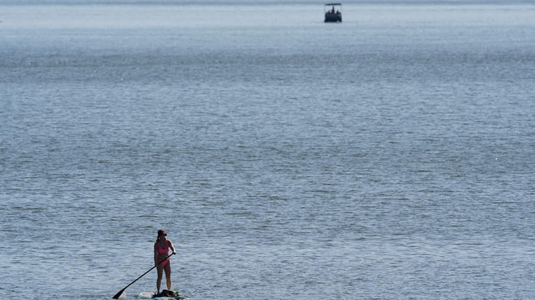 A woman rows her paddleboard as she takes advantage of...