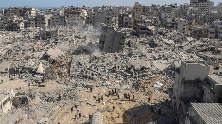 Palestinians walk through the destruction left by the Israeli air...