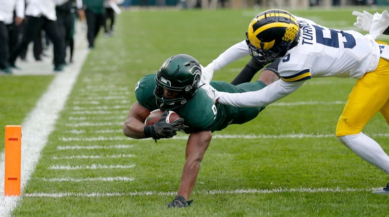 Michigan State's Kenneth Walker III, left, dives over the goal...