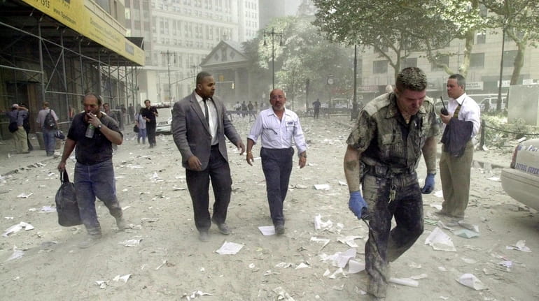 A police officer walks with others covered in dust during...