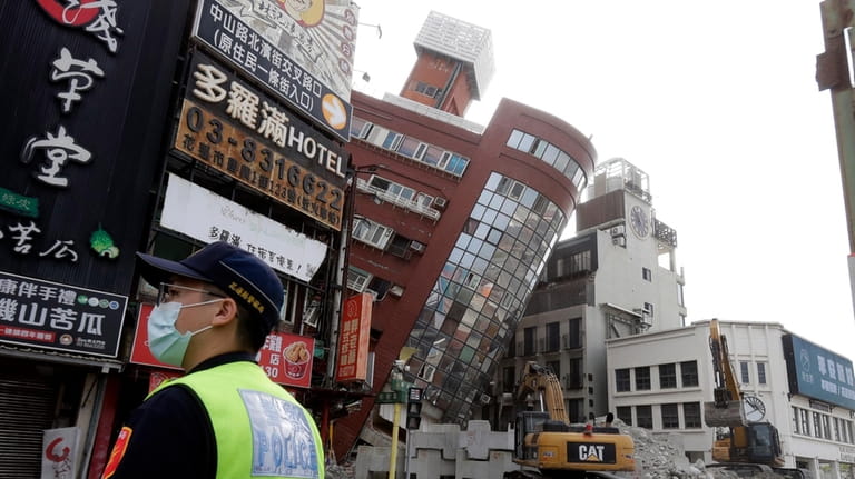 A police officer stands guard near a partially collapsed building...
