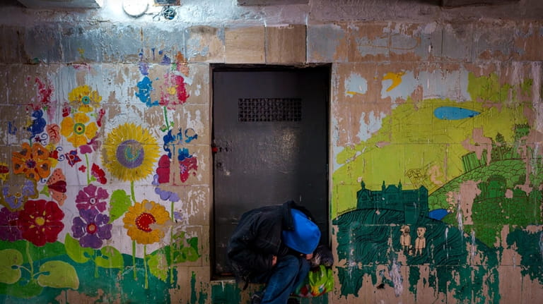 A person sits in an underpass with faded paintings on...