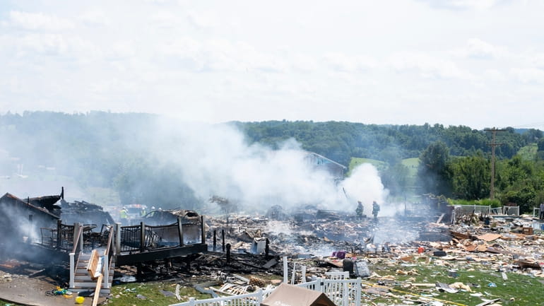 Two firefighters stand on the debris around the smoldering wreckage...