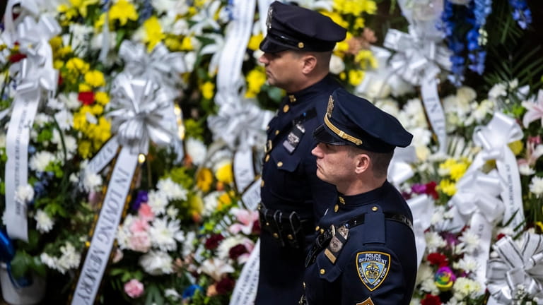 NYPD officers stand by flowers laid at the department's Tuesday...