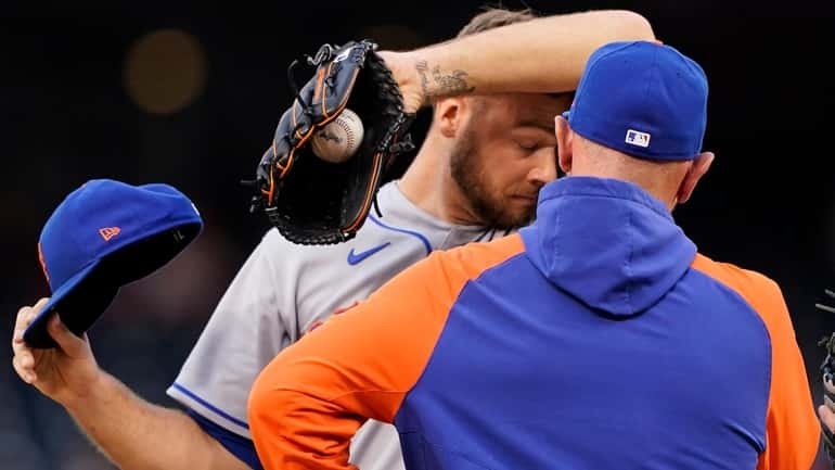 Mets starting pitcher Tylor Megill, left, wipes his face as...