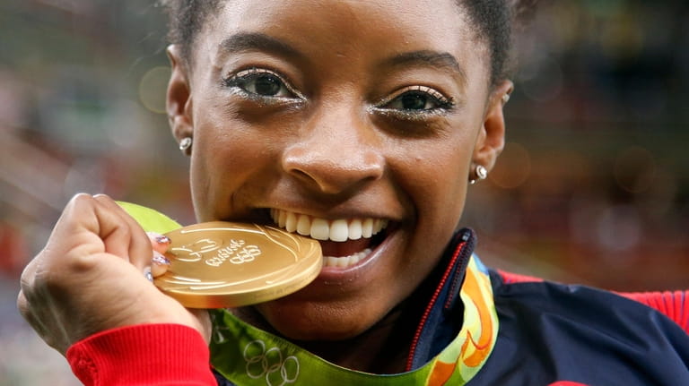 United States' Simone Biles bites her gold medal for the...