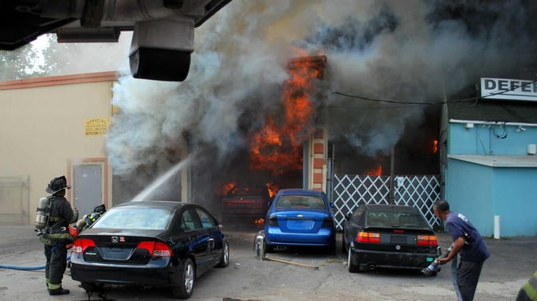 Firefighters battle the fire of an auto body shop in...