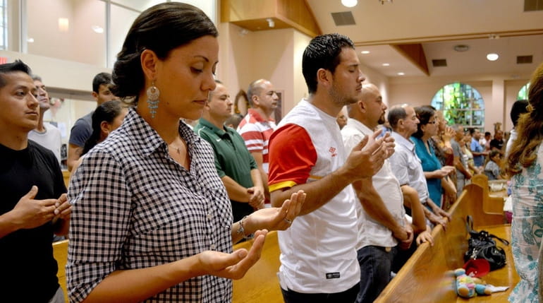 Parishioners raise their hands in prayer during a Spanish-language Mass...