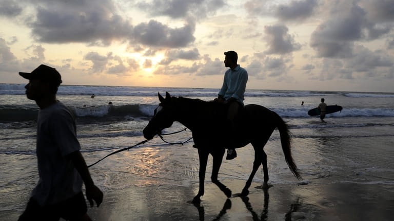 A tourist rides on a horse at Kuta beach on...