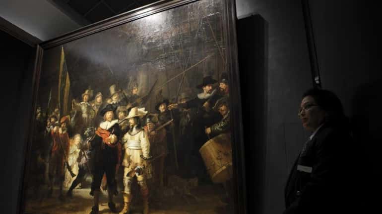 A security guard stands next to Rembrandt's "Night Watch" painting,...