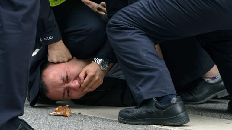 Chinese policemen pin down a protester and covered his mouth...