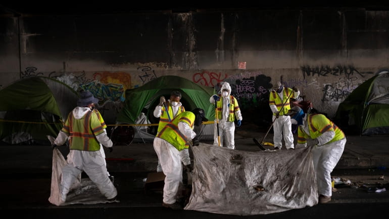 Los Angeles city employees clean up a homeless encampment to...