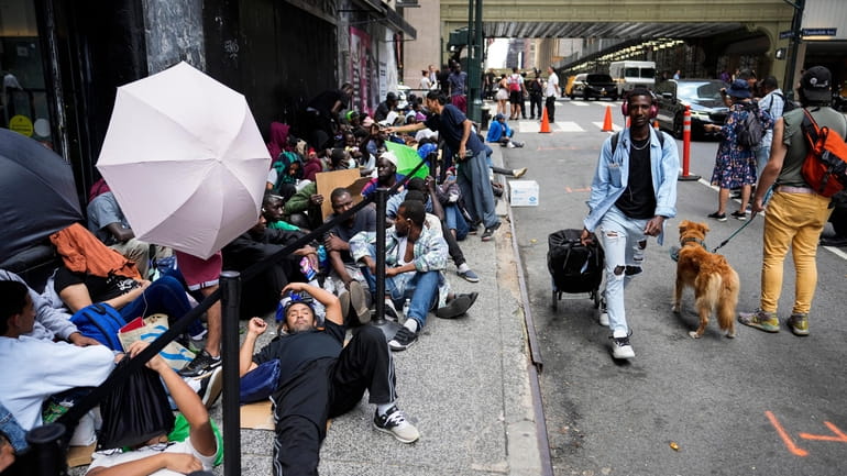 Migrants sit in a queue outside of The Roosevelt Hotel...