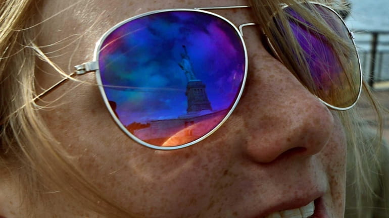 A tourist's sunglasses reflect Lady Liberty as the ferry approaches...
