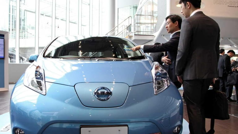 Visitors look at a Nissan Leaf electric car at the...
