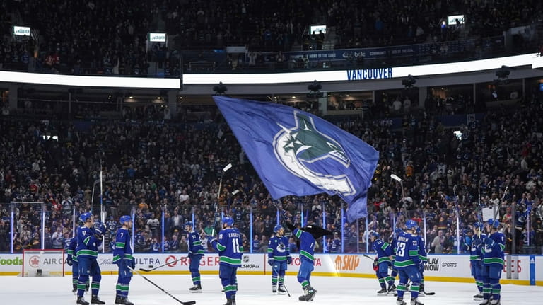 Vancouver Canucks players gather at center ice to raise their...