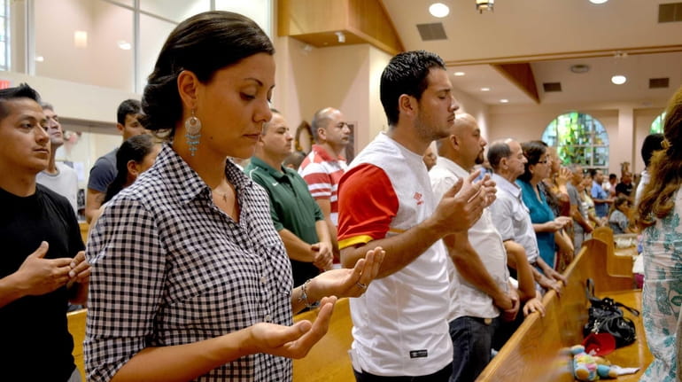 Parishioners raise hands in prayer during the Spanish-language Mass at...