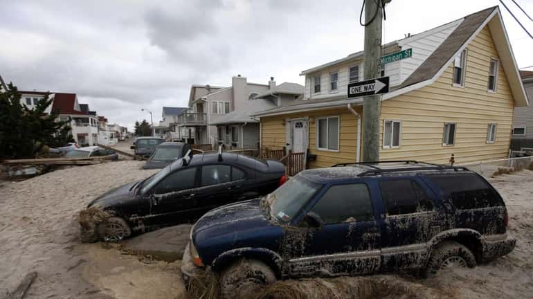 Cars lifted by floodwater from superstorm Sandy are mired in...