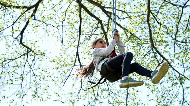 Sophia Luebker, 11, of Huntington, climbs a tree with the...