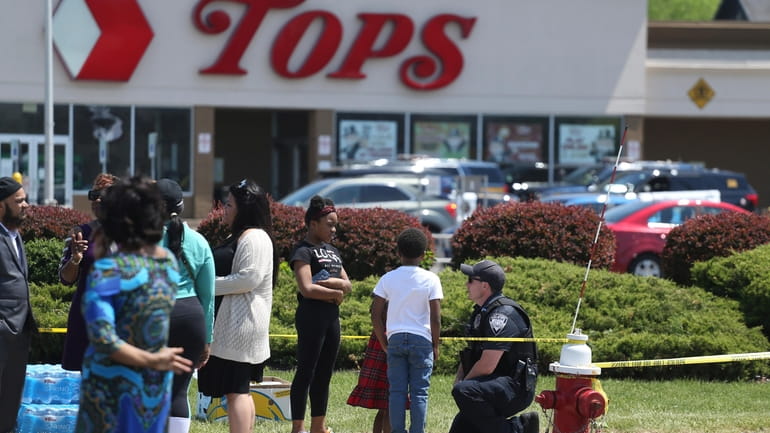 A Buffalo police officer speaks with children Sunday outside the Tops...