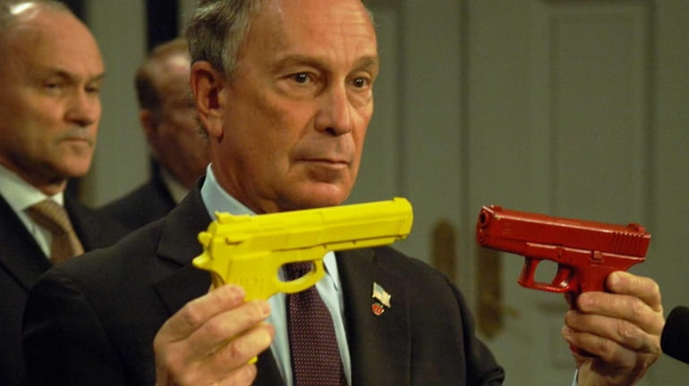 Mayor Michael Bloomberg holds two guns, one a toy, left,...