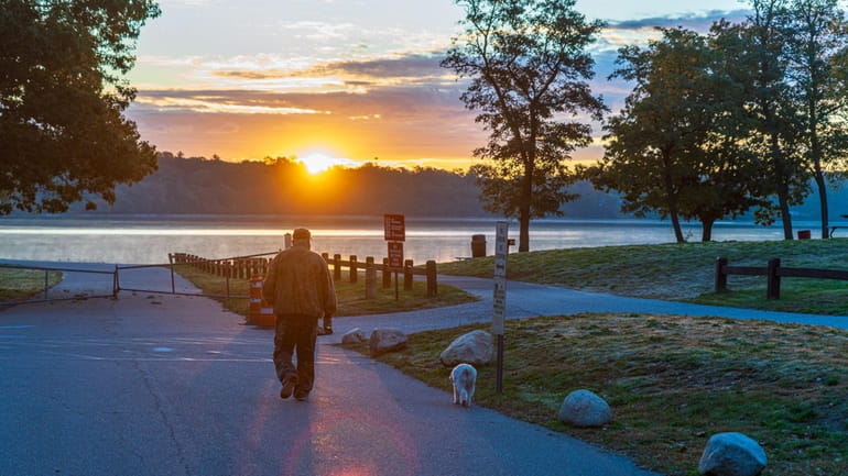 Bill Vorisek of Nesconset walks his dog Woody during Wednesday's sunrise over...