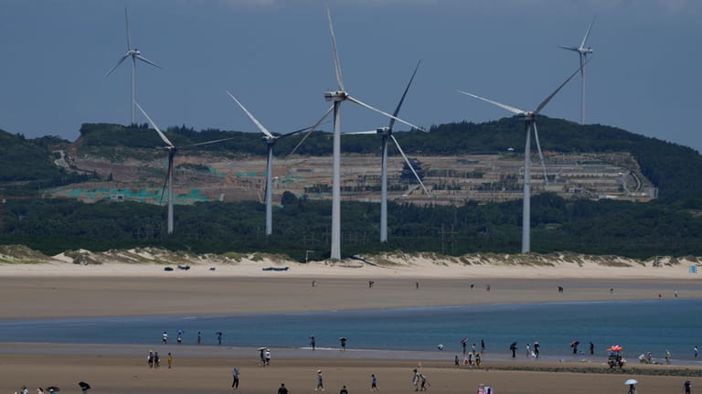 Beachgoers walk near wind turbines along the coast of Pingtan...