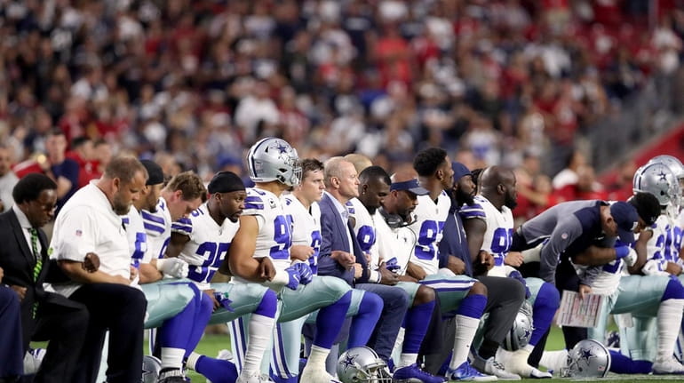 Members of the Dallas Cowboys link arms and kneel during...
