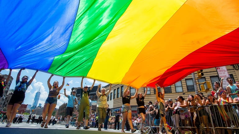 A large rainbow flag is carried up Seventh Avenue in...