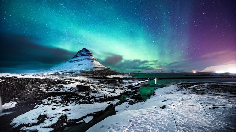 A traveler walking in front of the Northern Lights in...