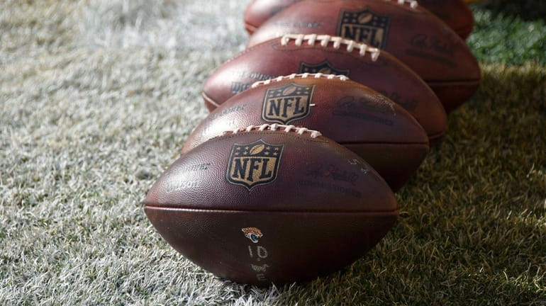 NFL footballs sit on the field during warm-ups before an...