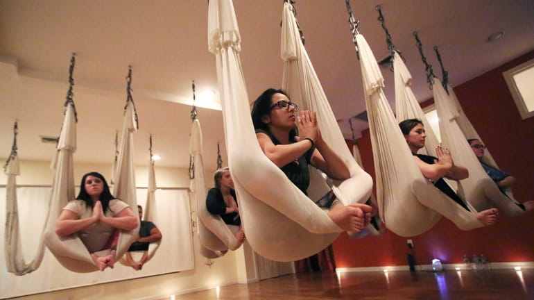Anti-gravity yoga participants assume yoga positions at Emerge Yoga and...