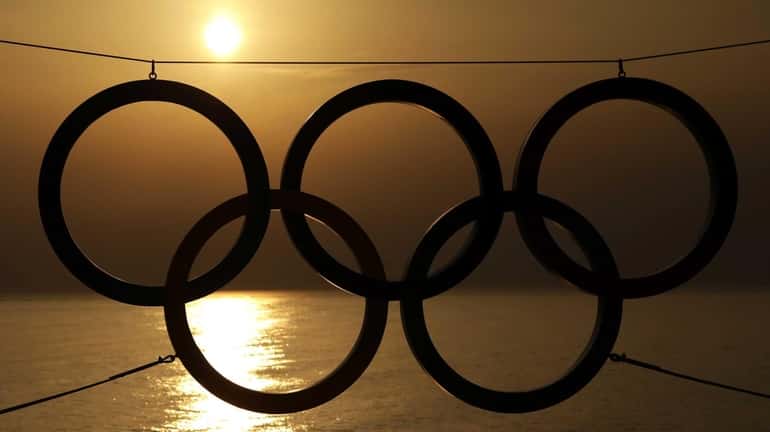 A set of Olympic Rings are silhouetted against the setting...