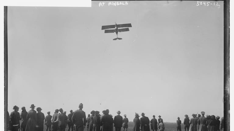 A single-seat biplane soars above the crowd at Roosevelt Field...