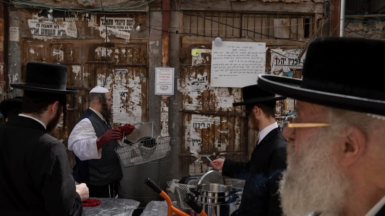 An ultra-Orthodox Jewish man dips cooking utensils in boiling water...