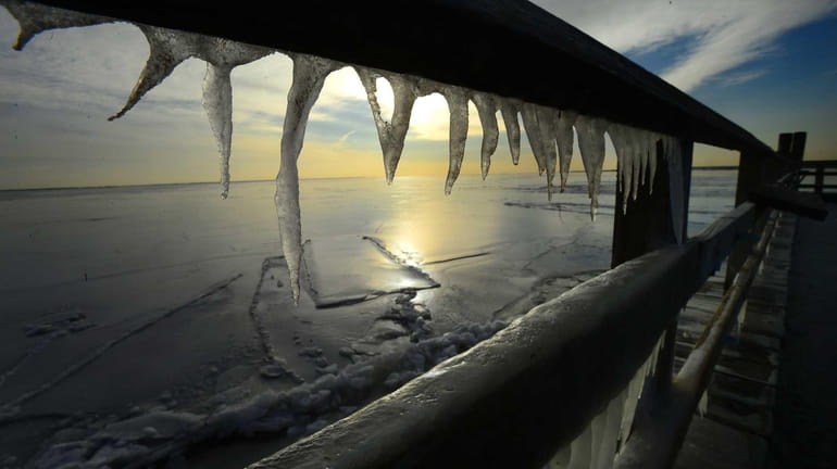 The frozen Great South Bay is viewed through icicles formed...