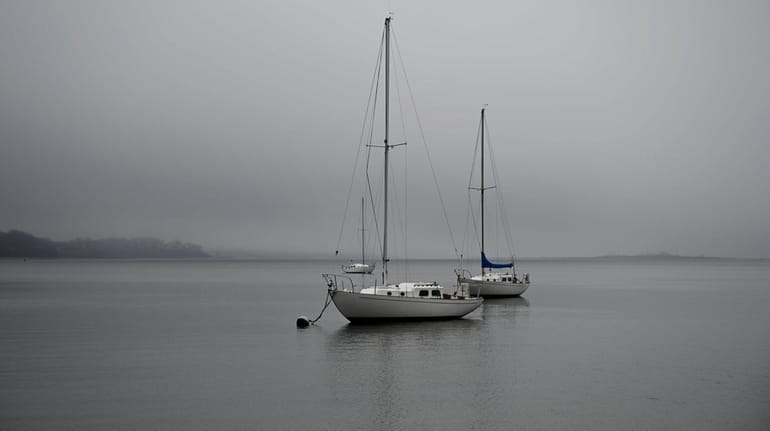 Sailboats are moored in Port Jefferson Harbor on a foggy...