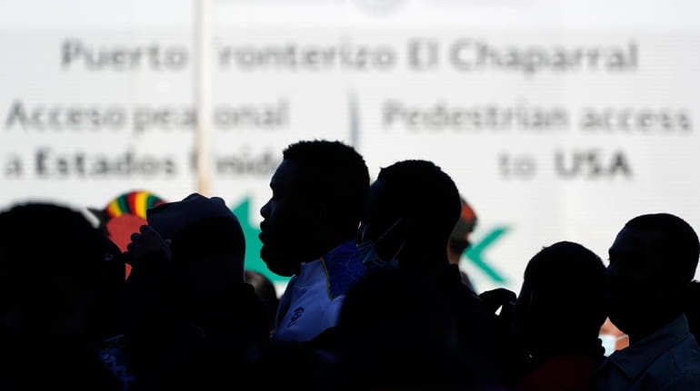 Asylum seekers waiting in Mexico stand in line at the...