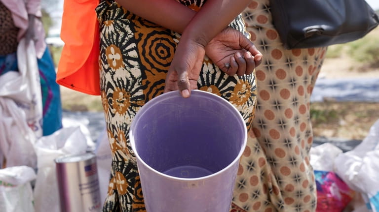 A woman holds an empty bucket while waiting to receive...