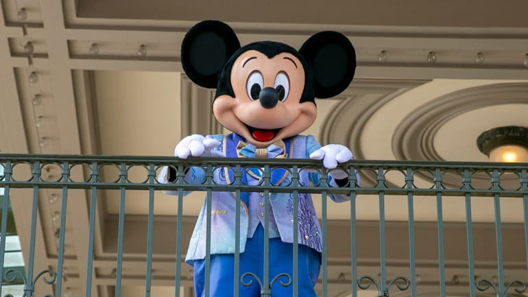 An actor dressed as Mickey Mouse greets visitors at the...