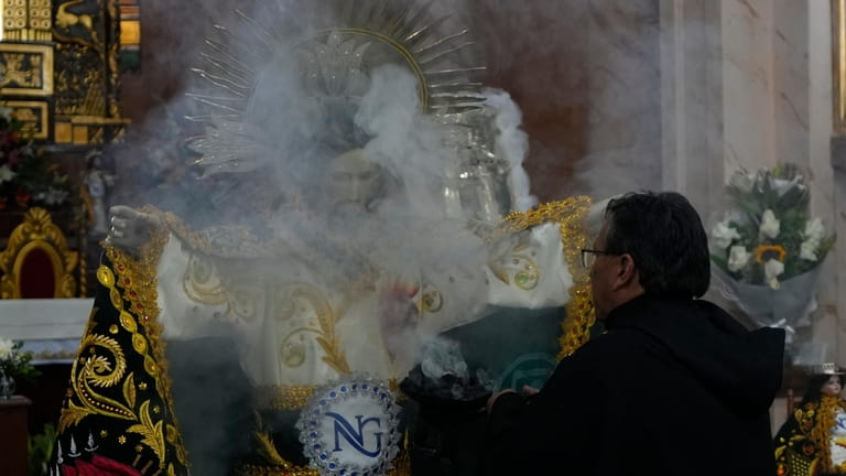 A priest releases incense after dressing the statue of "Jesus...