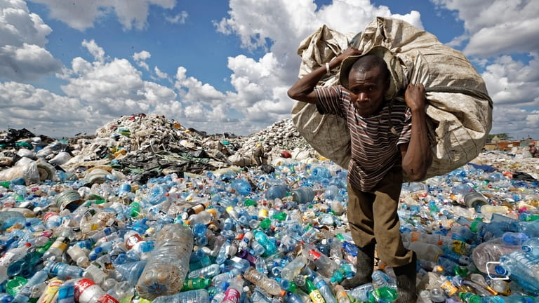 A man walks on a mountain of plastic bottles as...