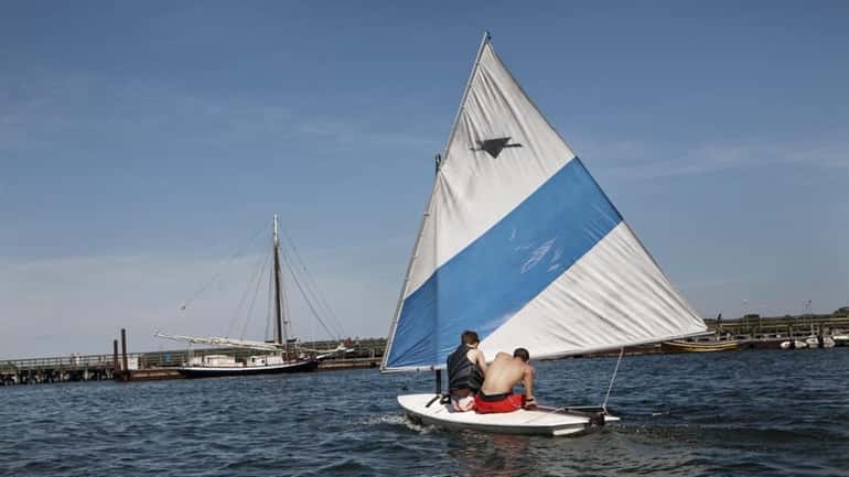 Two young men take a sailboat into the harbor in...