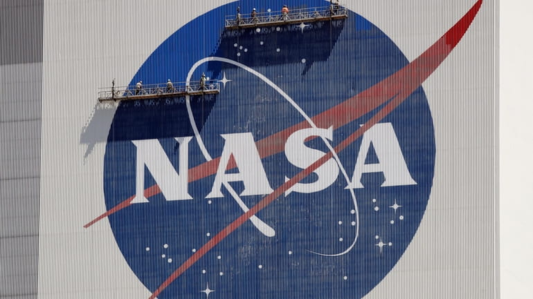 Workers on scaffolding repaint the NASA logo near the top...