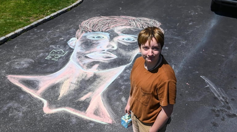 Nate Kane, 17, draws a face on the driveway of...