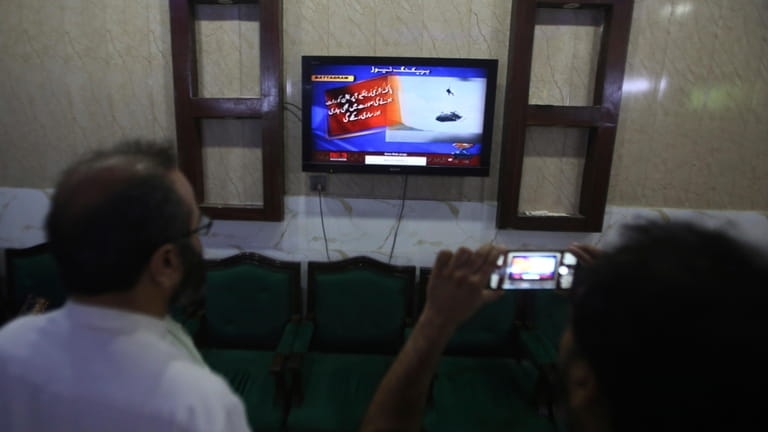 Members of media watch a news channel airing news regarding...