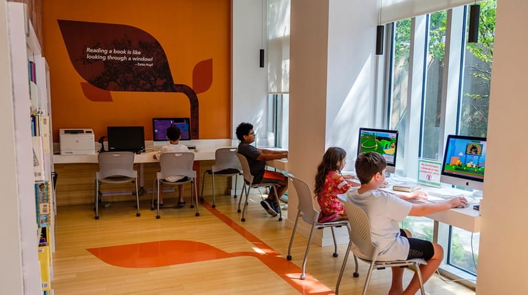 Children work on computers in a quiet study area in...